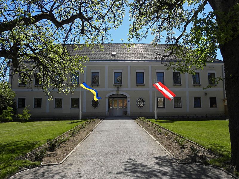 Zámok Hochwolkersdorf s dvoma vlajkami, obklopený stromami a trávnikom.