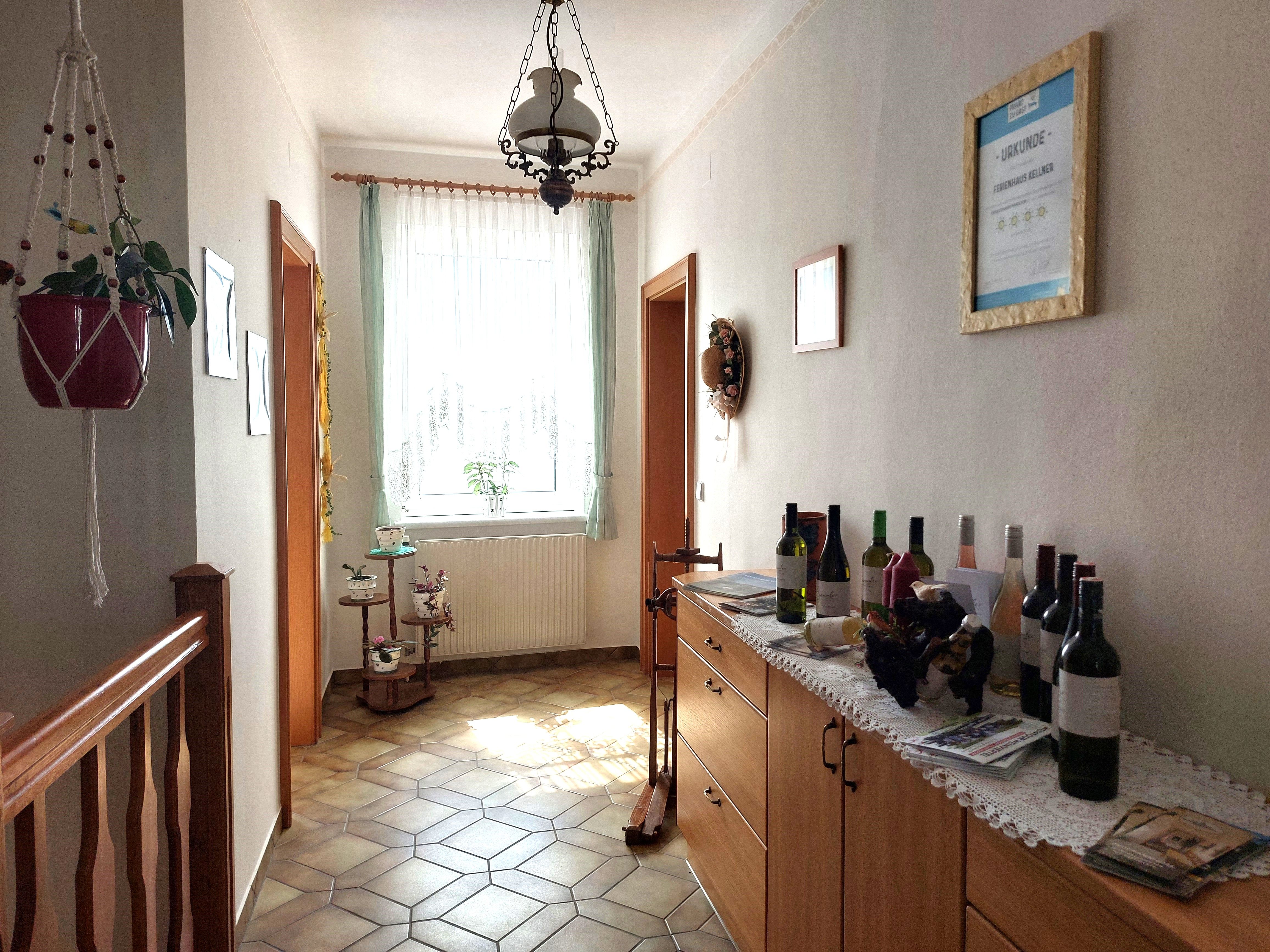 Svetlá predsieň s dláždenou podlahou, komodou s fľašami na víno a oknom so závesmi.
