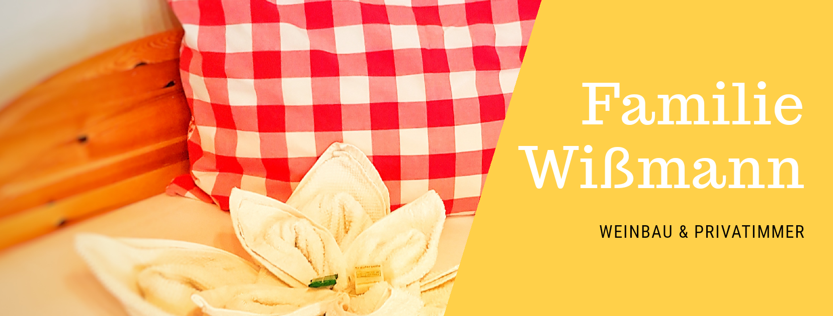 Červený vankúš so šachovnicovým vzorom a uterák v tvare kvetu na posteli. Text: Wißmann, vinohradníctvo a súkromné izby.