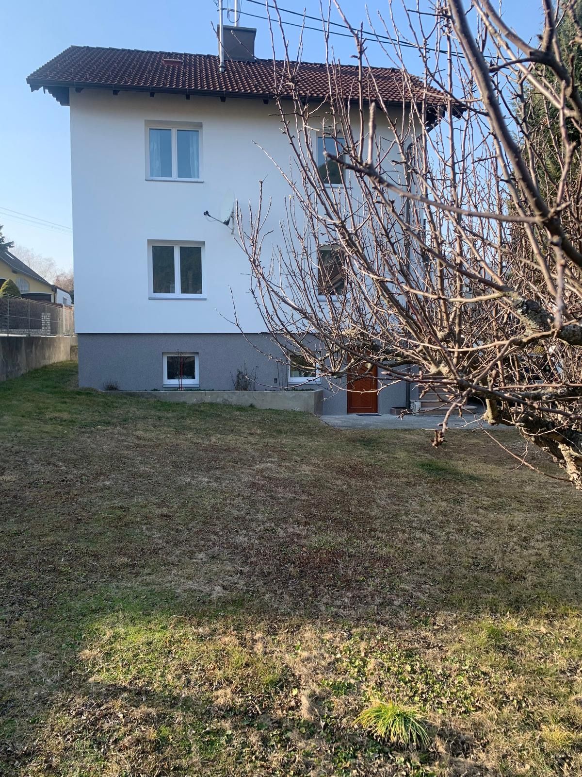Pohľad zvonku na biely dom s červenou strechou a záhradou.