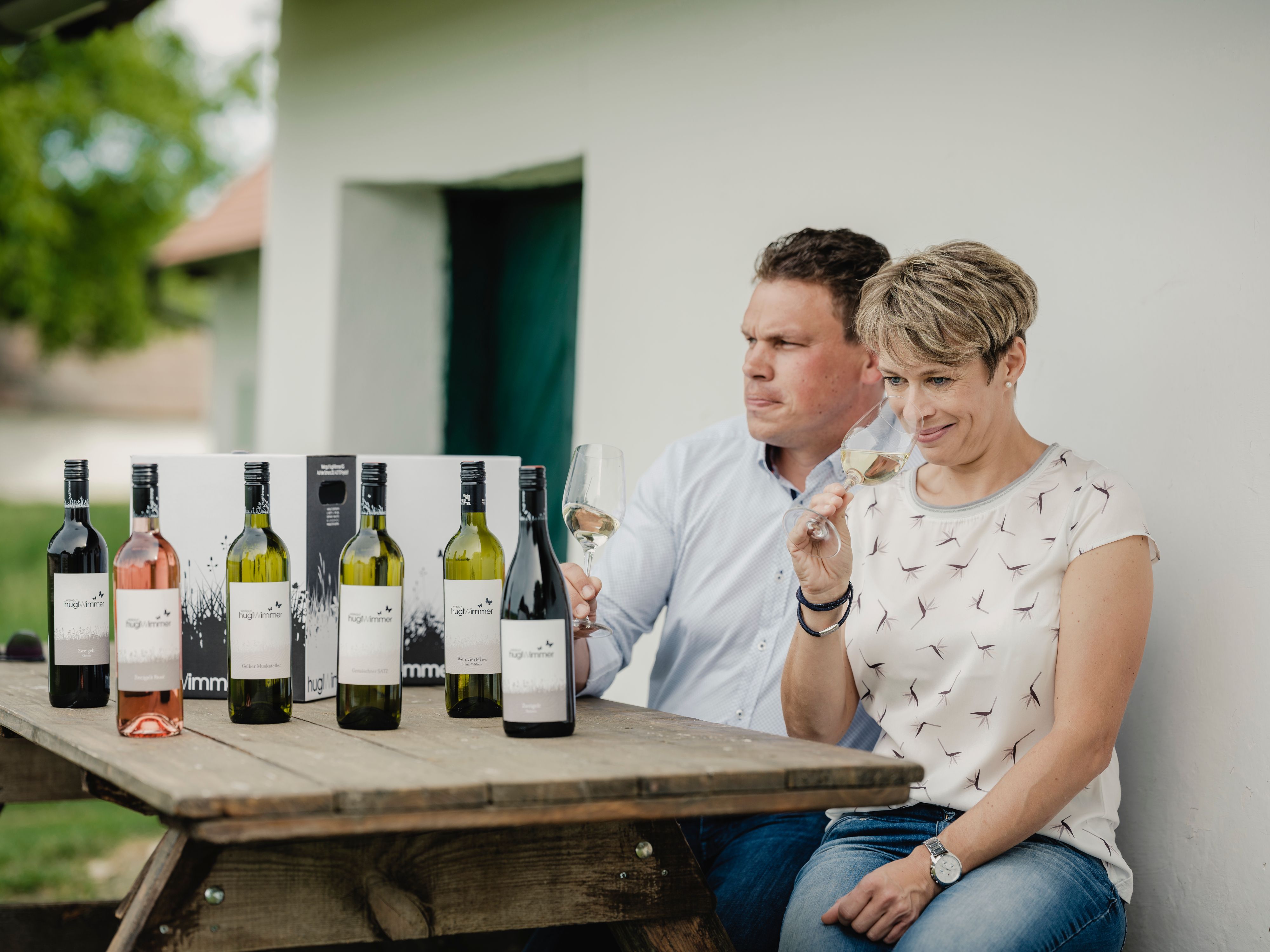 Dvaja ľudia sedia pri stole s fľašami vína a ochutnávajú víno.