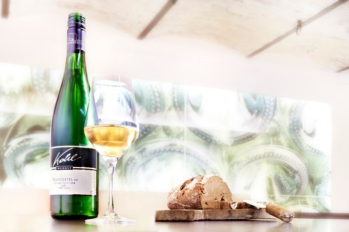 Fľaša bieleho vína, naplnený pohár a bochník chleba na stole.