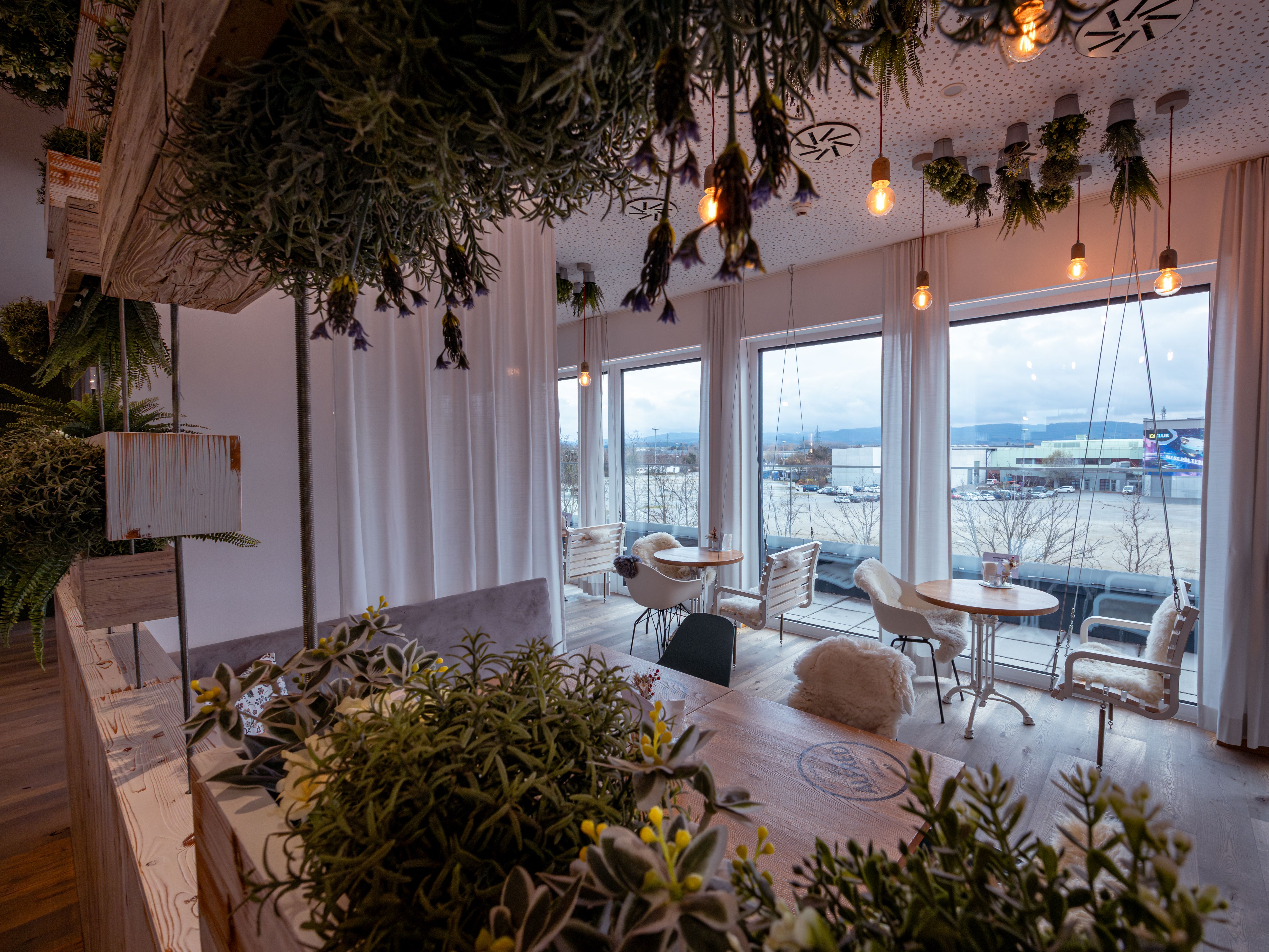 Moderná hotelová izba s manželskou posteľou, dreveným obložením a oknami so závesmi.