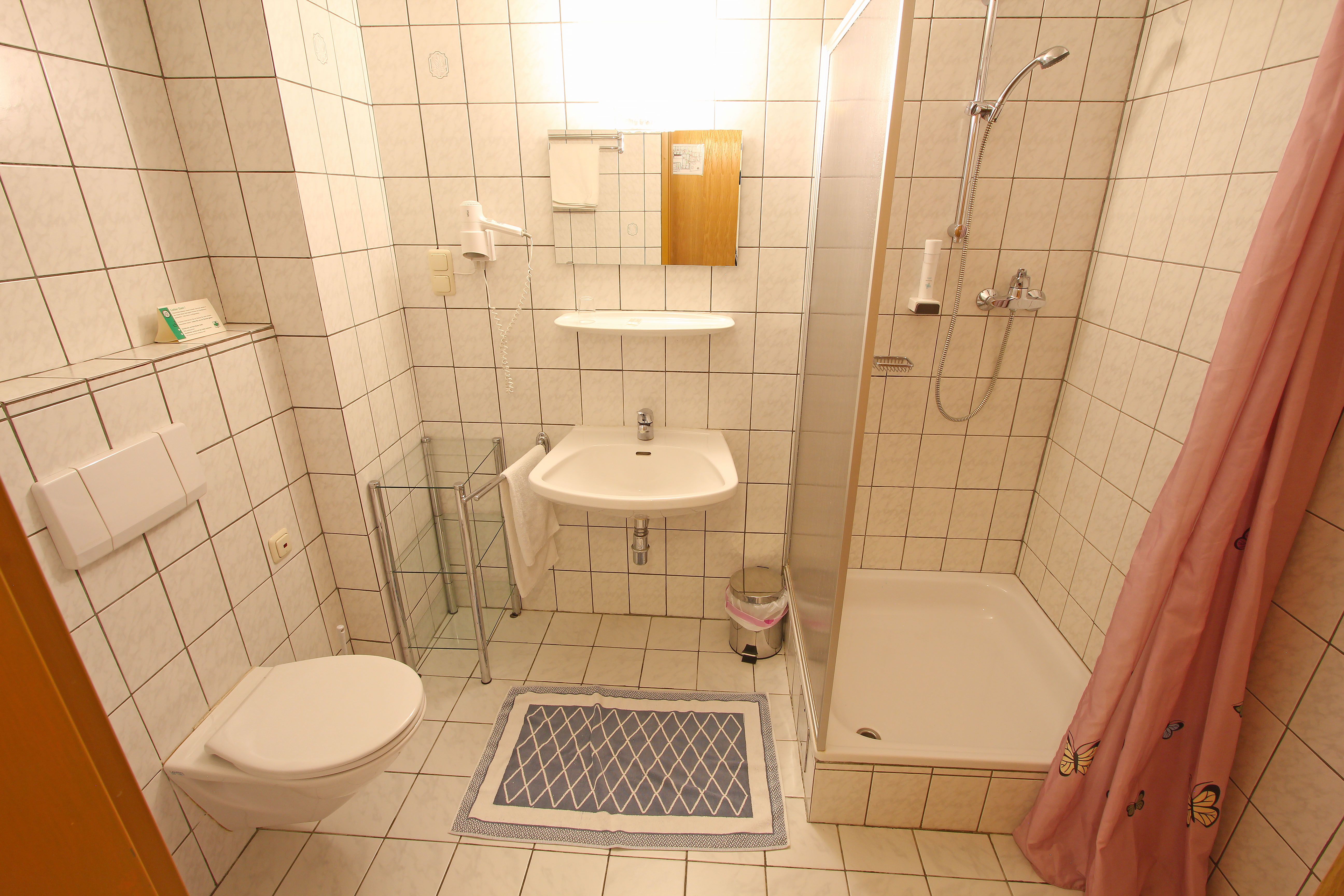 Malá kúpeľňa so sprchovacím kútom, umývadlom a toaletou, obložená bielymi dlaždicami.