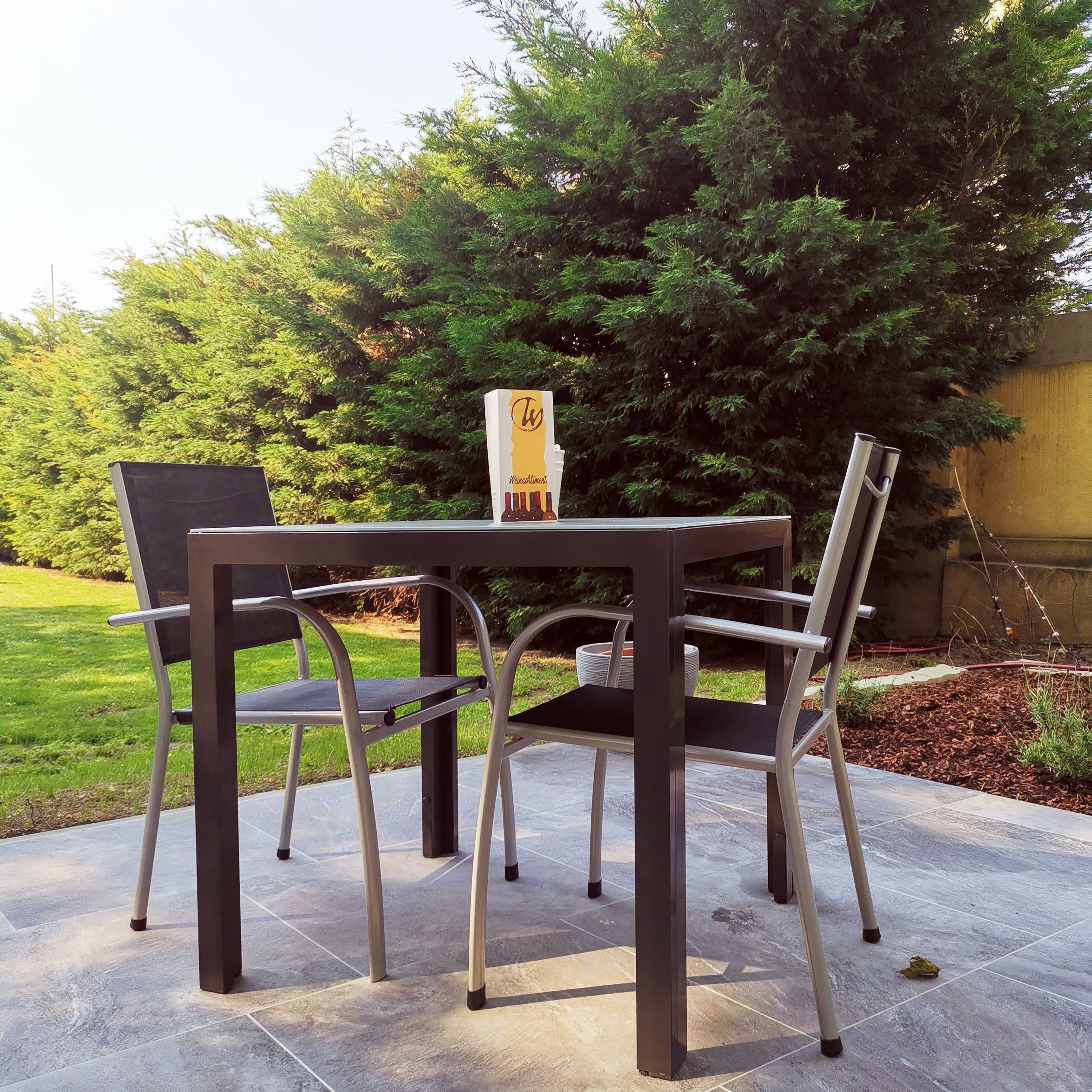 Terasa so stolom, dvoma stoličkami a stromami v pozadí.