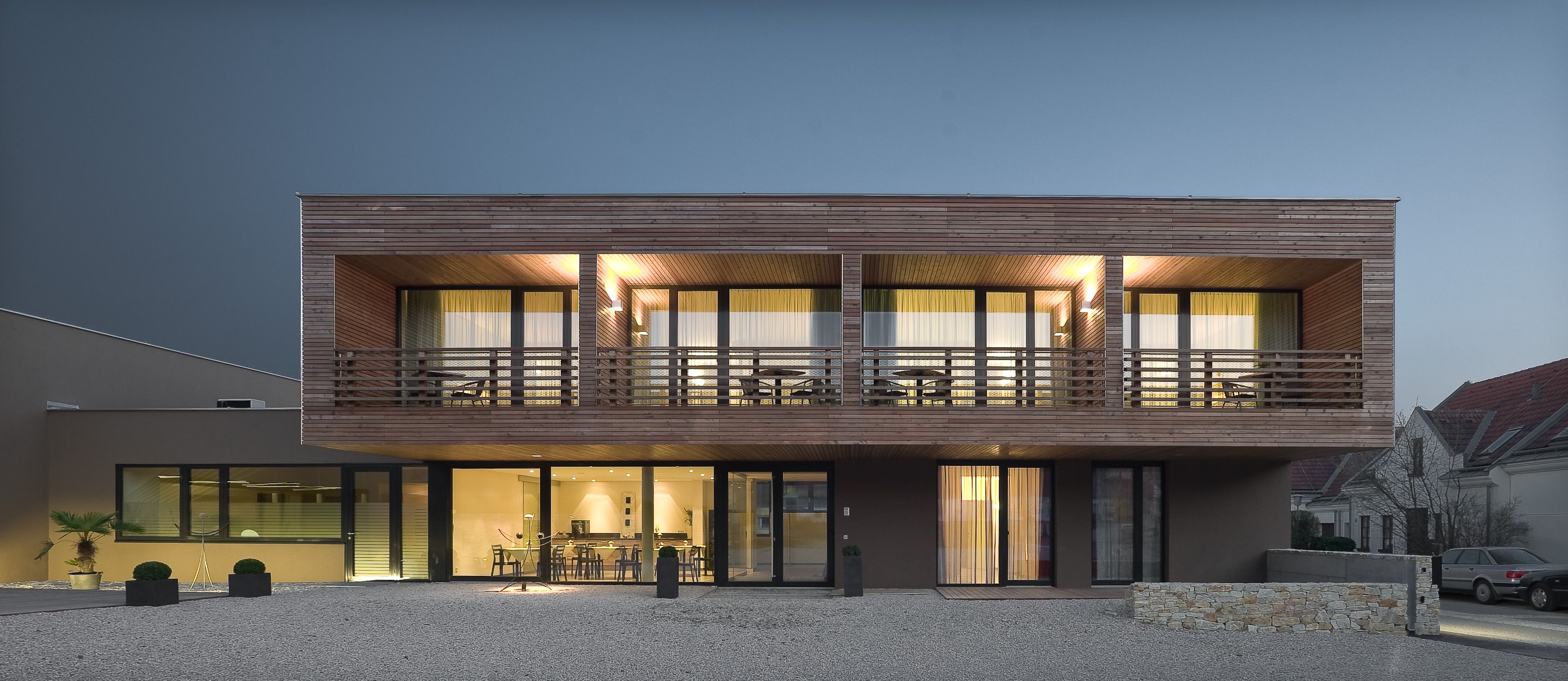 Moderný dvojpodlažný dom s dreveným obložením a veľkými oknami s nočným osvetlením.