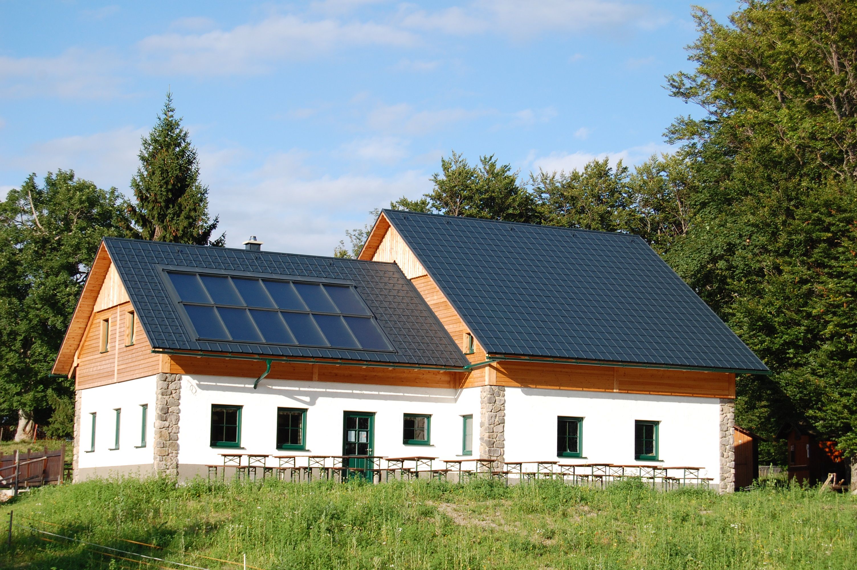Chata so solárnymi panelmi na streche, obklopená stromami a lúkami.