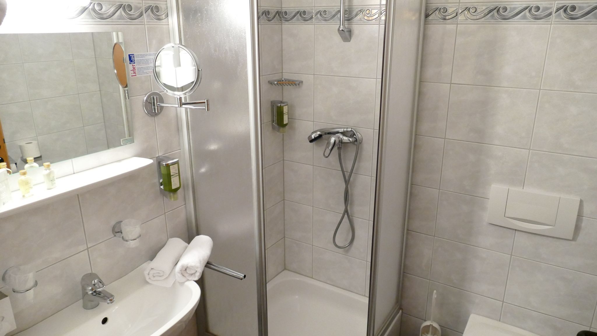 Kúpeľňa so sprchovacím kútom, umývadlom a zrkadlom.