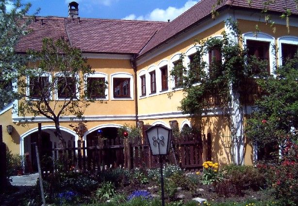 Žltý dom s červenými škridlami a záhradou v popredí.