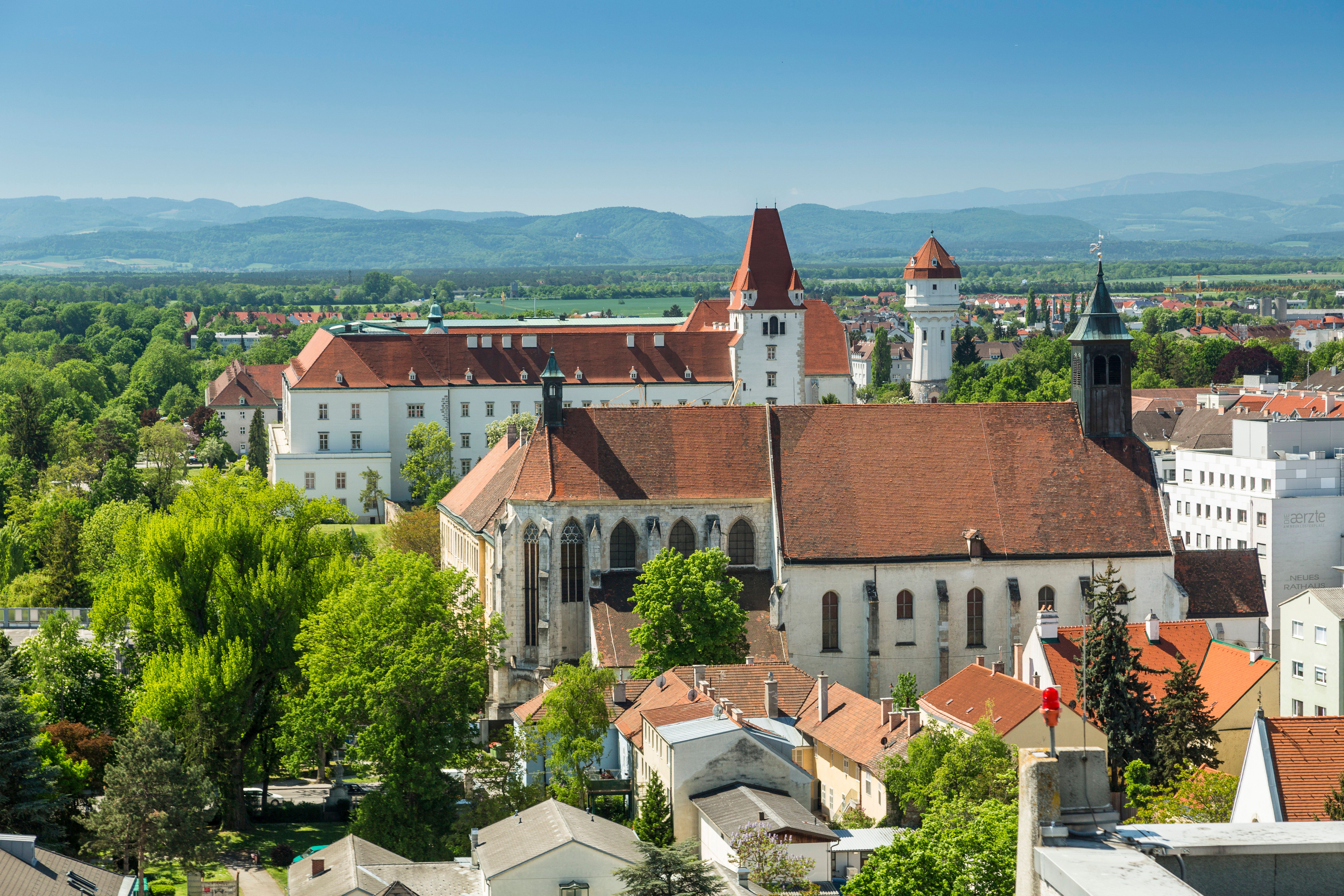 Tri pamiatky na jednej fotografii: Kláštor Neukloster, Teréziánska vojenská akadémia v Akademieparku a vodná veža. V pozadí sú hory Viedenských Álp.