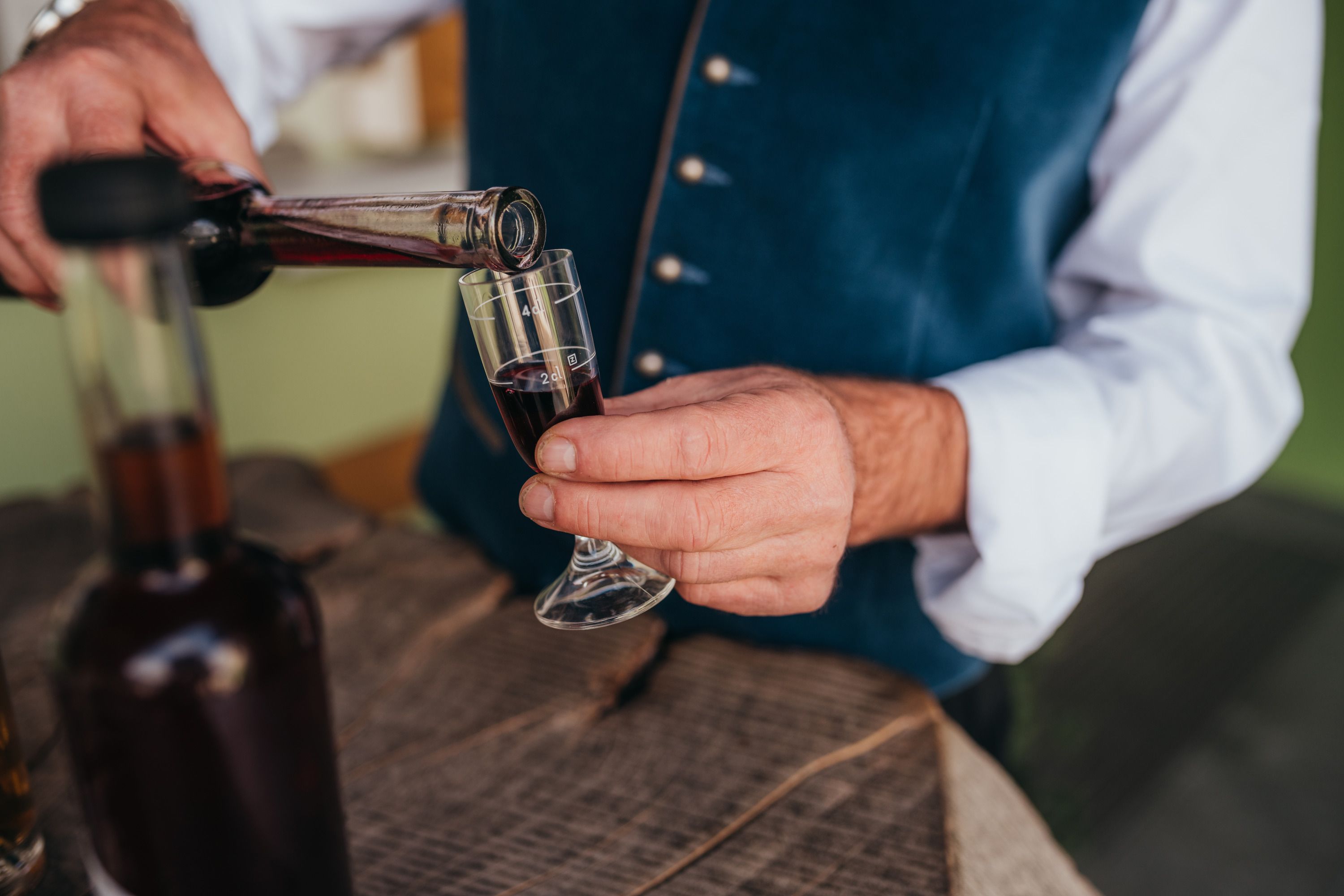 Osoba naleje červený likér do malého pohára.