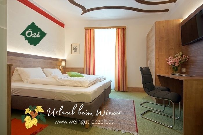 Útulná izba pre hostí s manželskou posteľou, písacím stolom a stoličkou, zdobená kvetmi. Svetlé závesy a podlaha s kobercom.