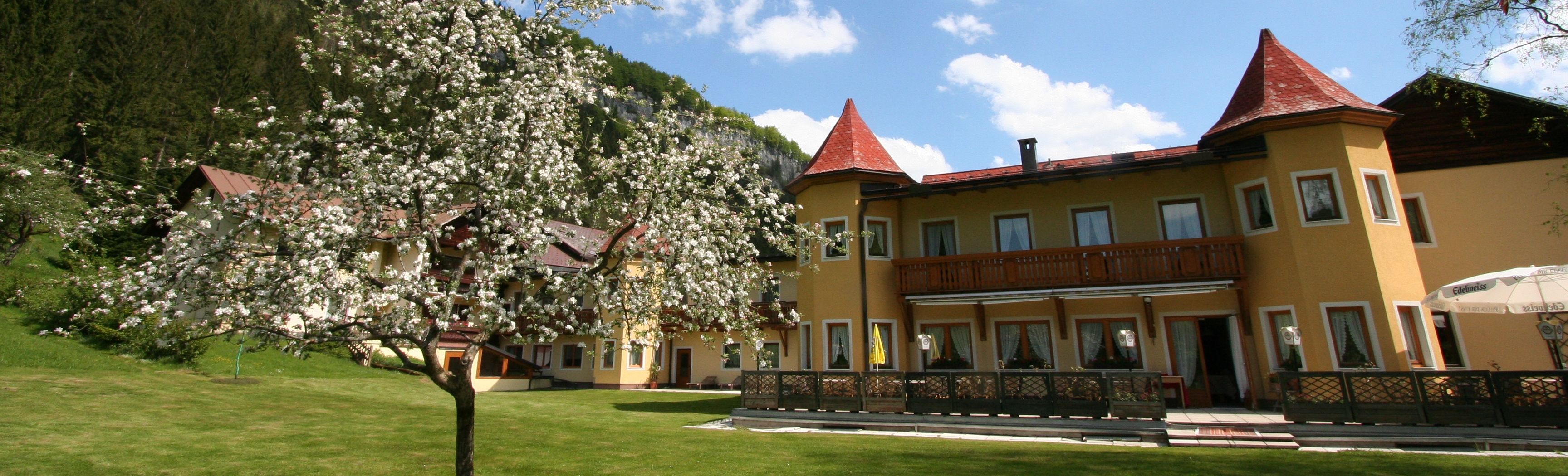 Žltý hotel s červenými strechami a rozkvitnutým stromom v popredí.