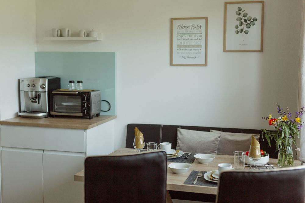 Malá kuchyňa s kávovarom, rúrou, jedálenským stolom a kvetmi.