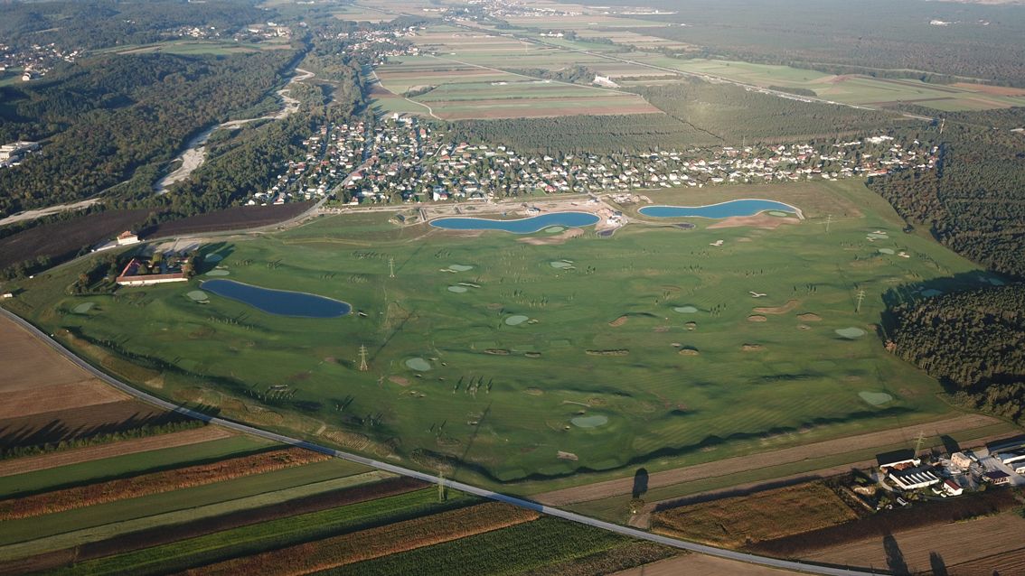 Letecký pohľad na golfové ihrisko s niekoľkými vodnými prekážkami a susednú osadu.