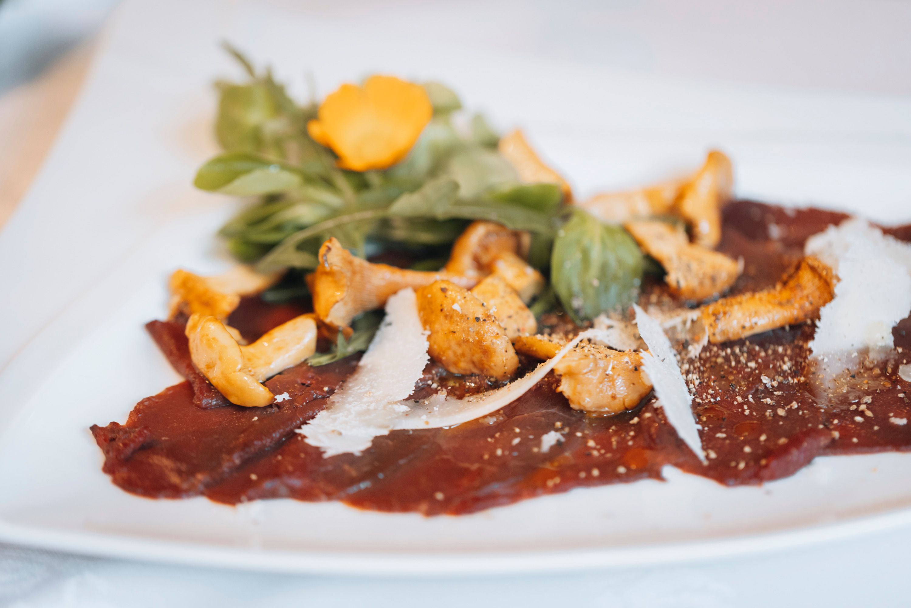 Carpaccio z daniela s nakladanými liškami a rukolou na bielom tanieri.