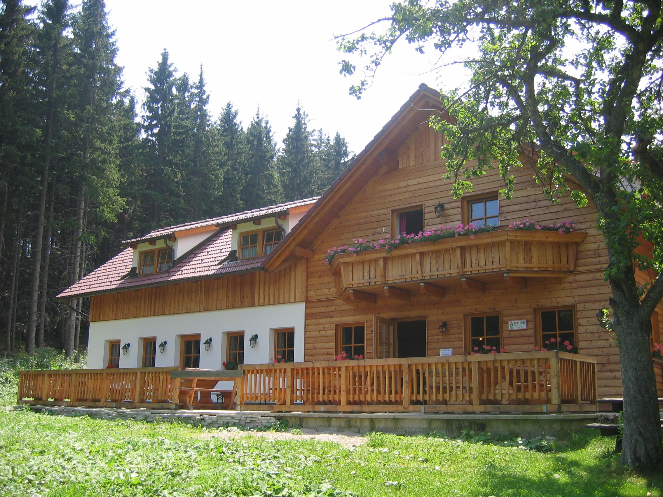 Rustikálna drevená horská chata s balkónom a terasou, obklopená stromami.