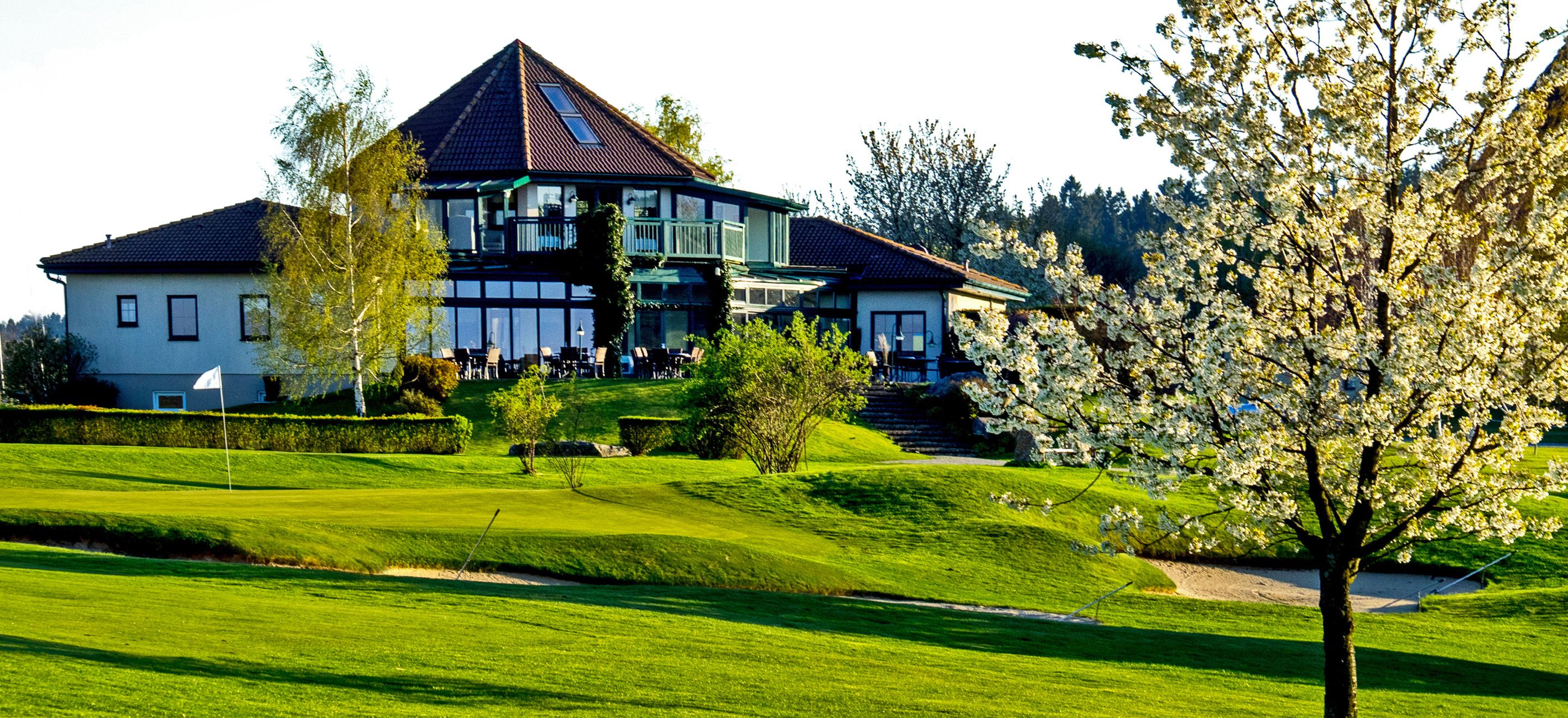 Klubovňa golfového klubu Ottenstein s kvitnúcim stromom v popredí.