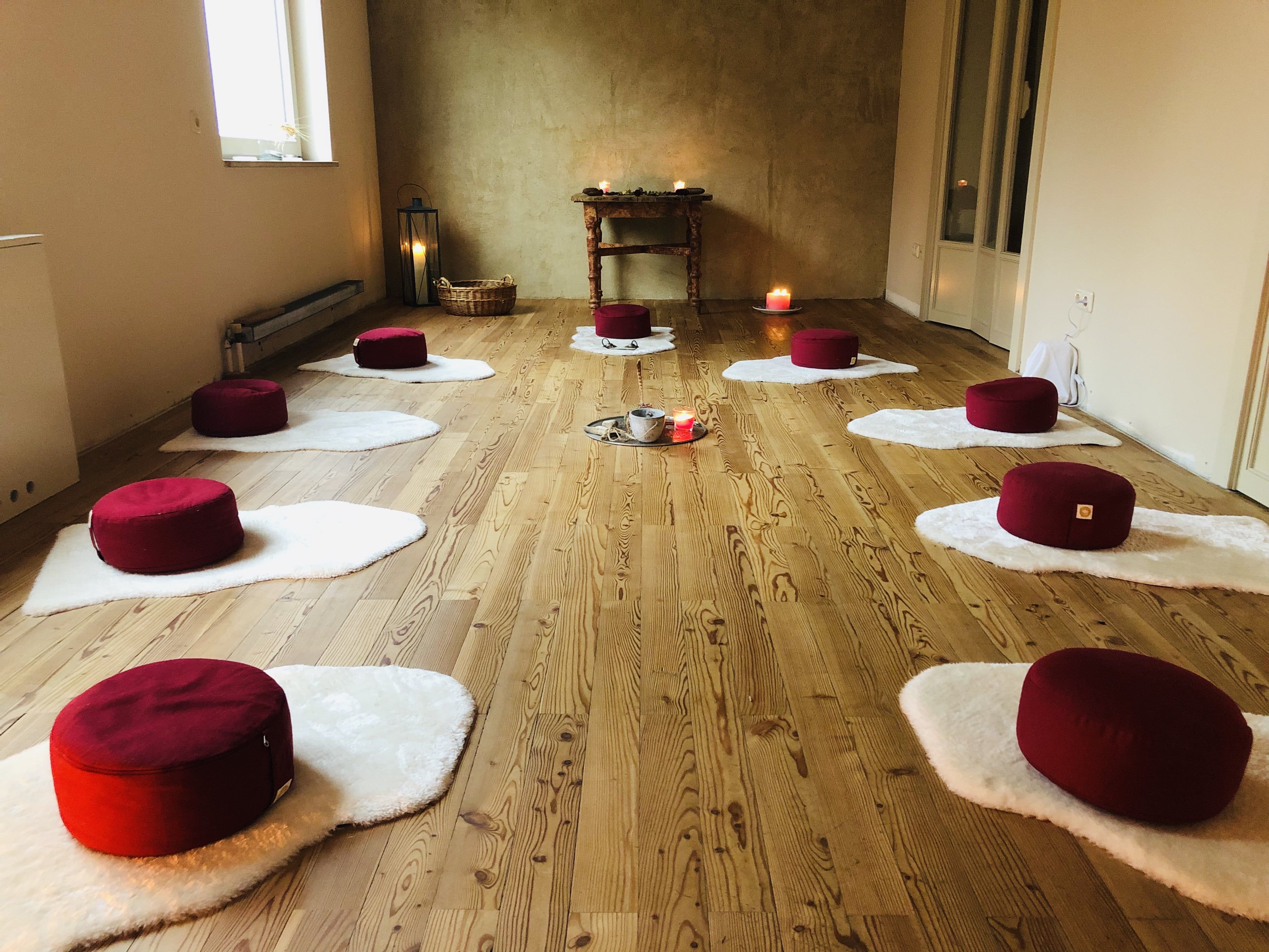 Meditačná miestnosť s červenými vankúšmi na bielych rohožiach, sviečkami a drevenou podlahou.