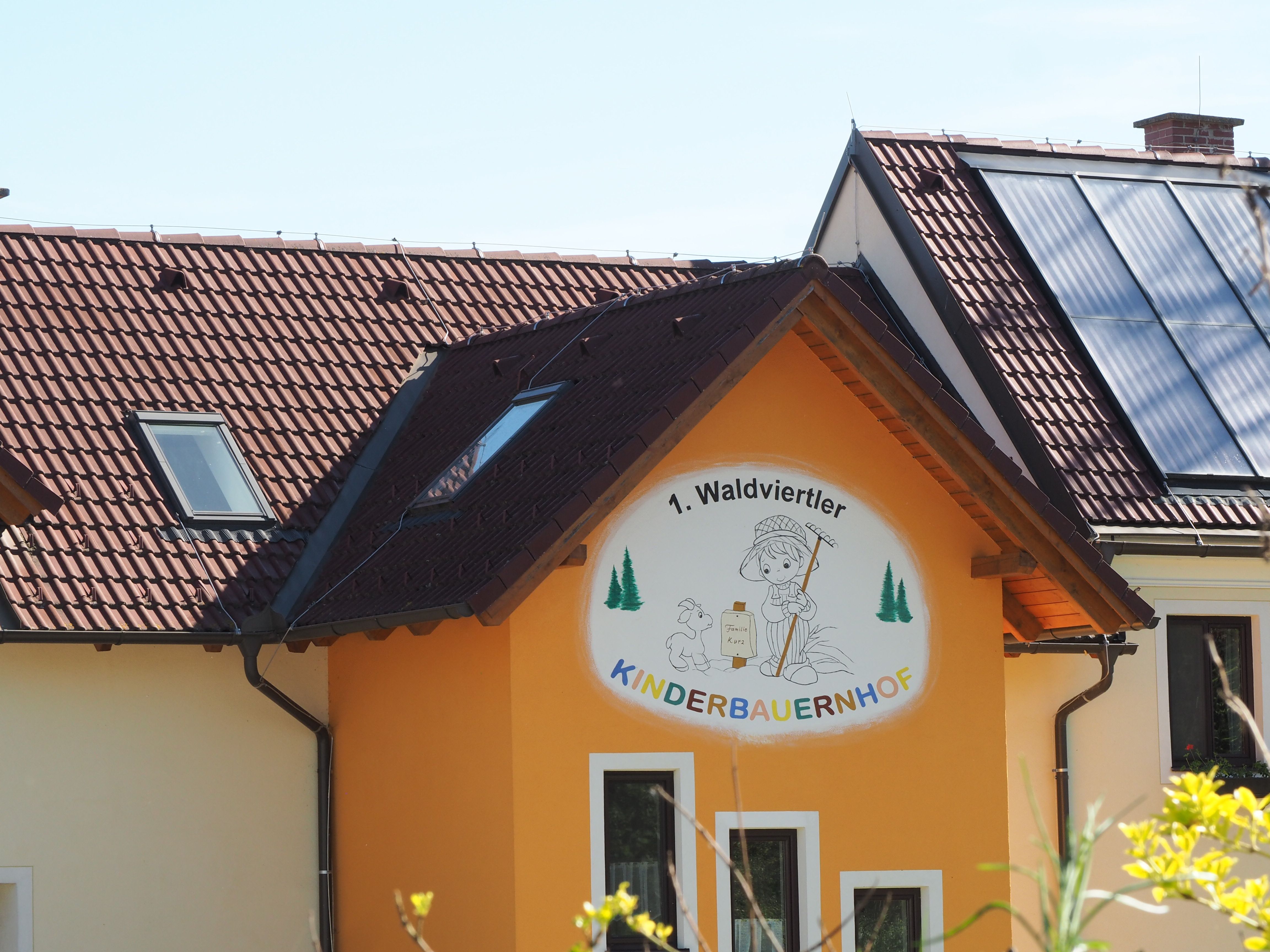 Budova s nápisom "1. Waldviertler Kinderbauernhof", solárne panely na streche.