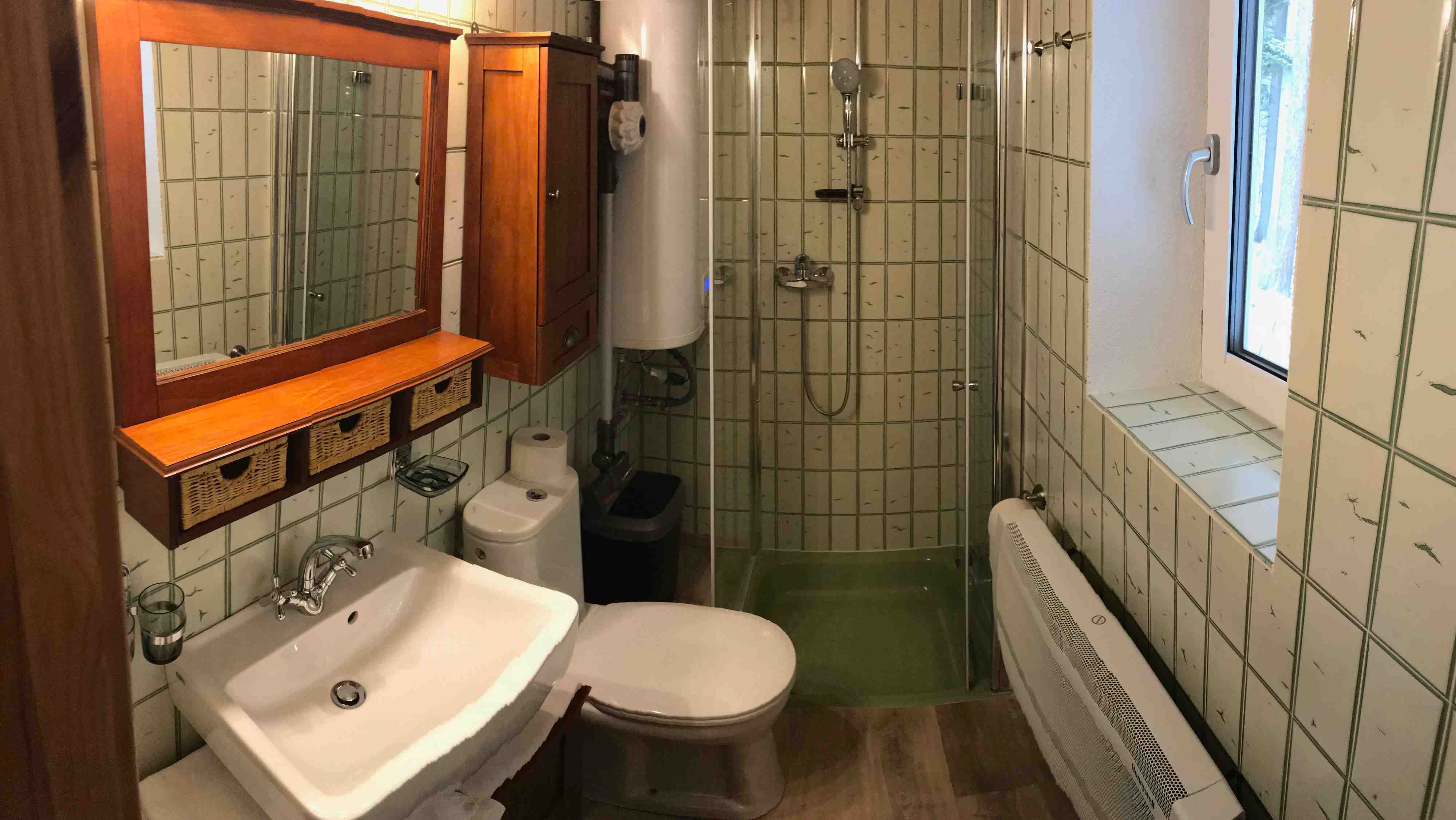 Malá kúpeľňa so sprchovacím kútom, umývadlom, WC a drevenými skrinkami.