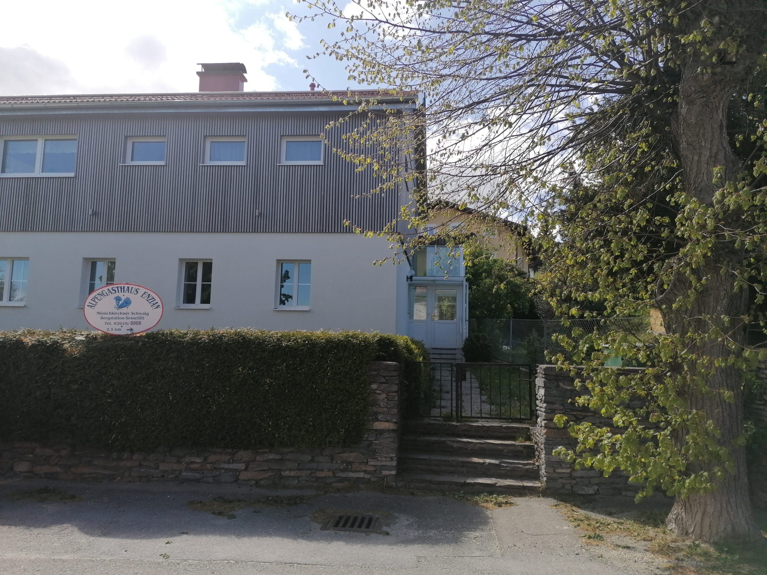 Dvojpodlažná budova s nápisom "Alpengasthaus Ewin" a záhradou.
