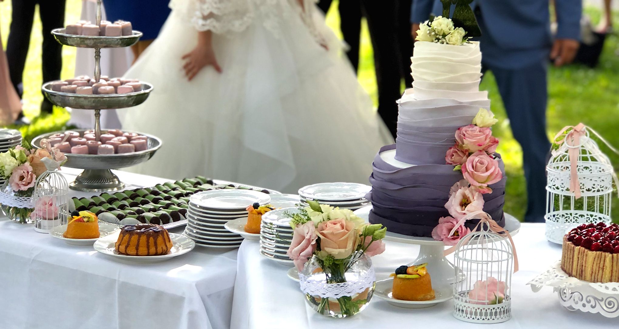 Svadobná torta a zákusky na vonkajšom stole s nevestou a ženíchom.