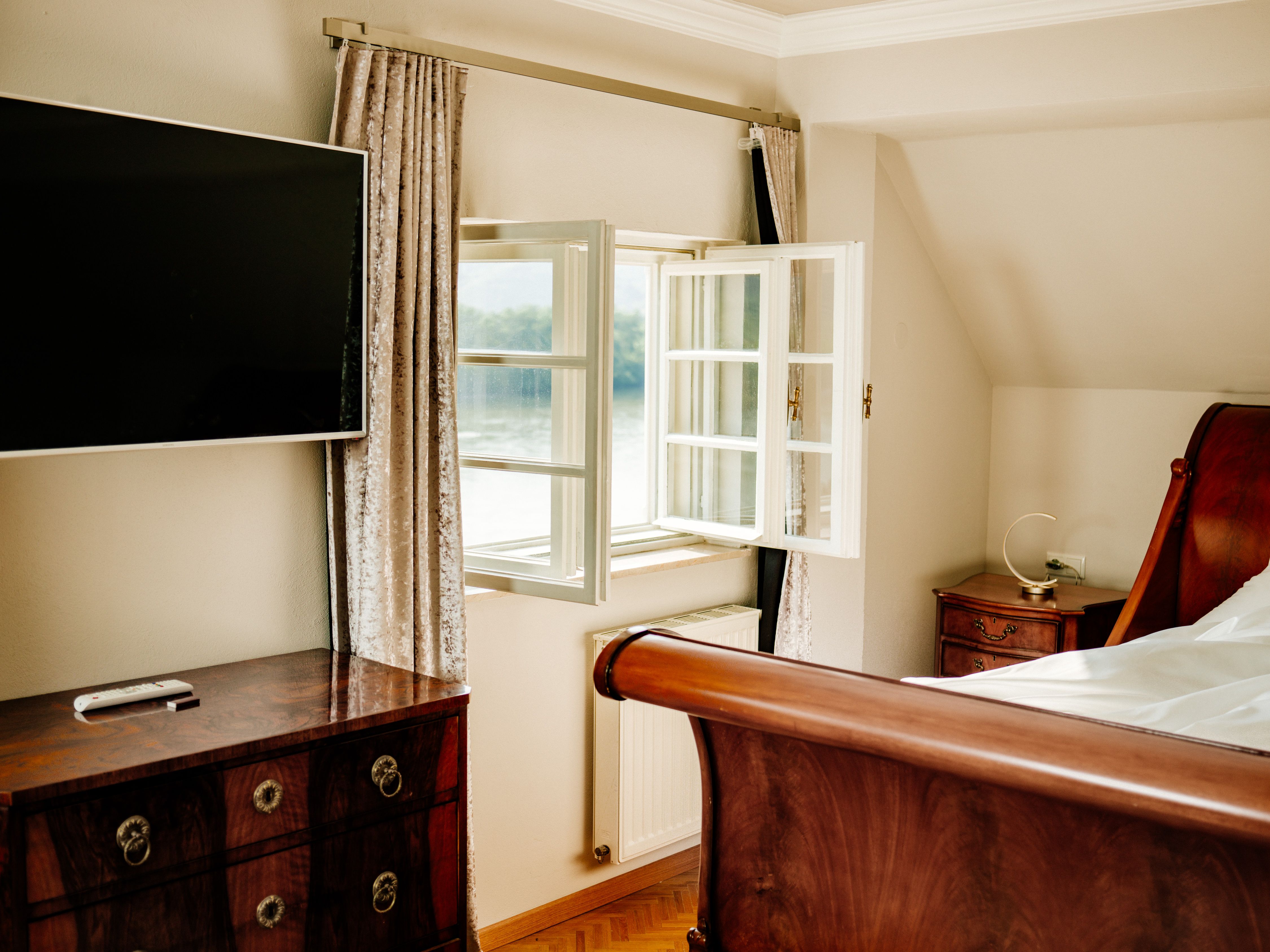 Elegantná spálňa s otvoreným oknom, TV s plochou obrazovkou, drevenou posteľou a starožitným nábytkom.