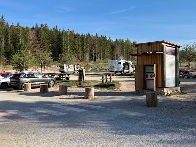 Parkovisko pri centre prírodného parku Hohe Wand s autami a karavanmi, obklopené lesom.