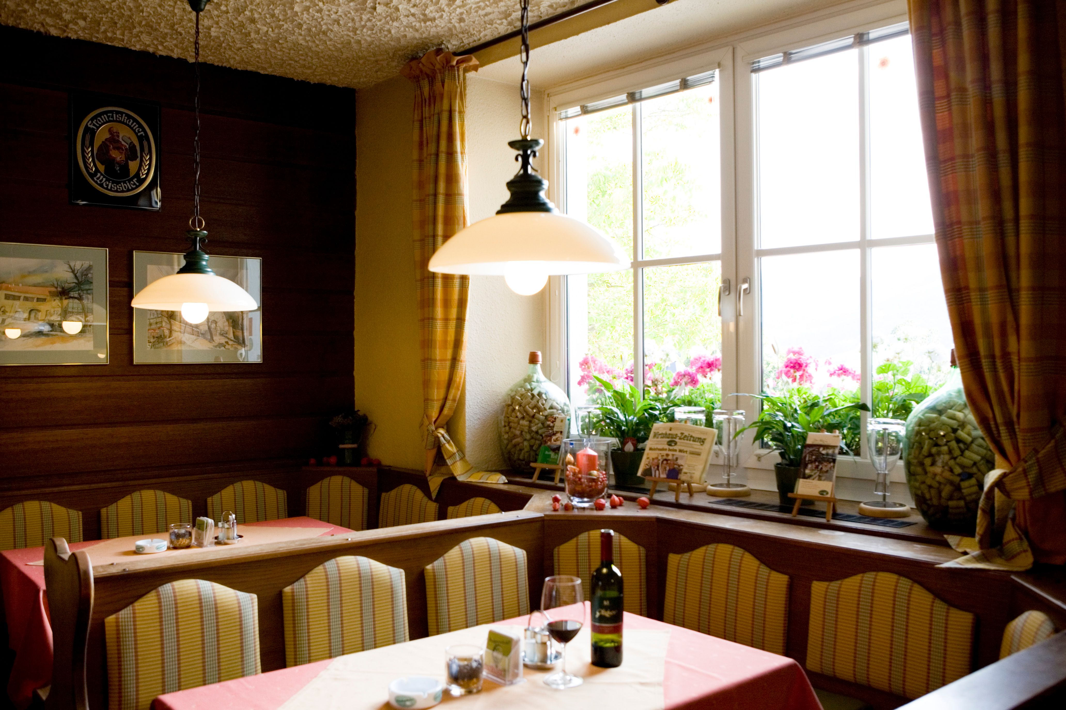 Útulná jedáleň s lavicami, stolmi, lampami a veľkým oknom so závesmi.