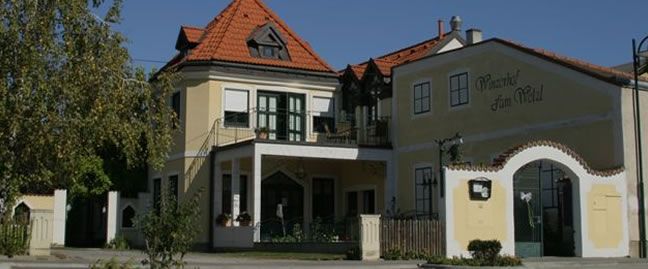 Tradičná budova so žltou fasádou a červenou škridlovou strechou s označením "Winzerhof zum Wald".