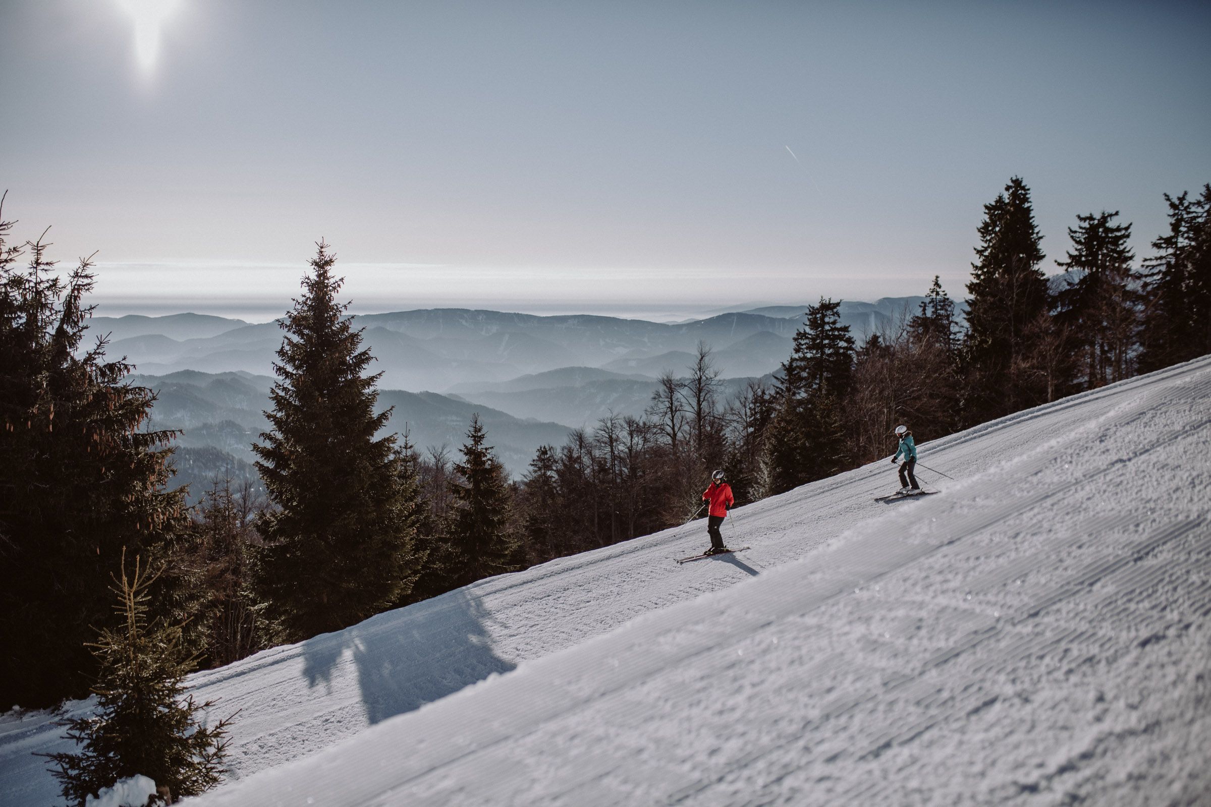 Dvaja lyžiari na zjazdovke v lyžiarskej oblasti Unterberg s horskou panorámou v pozadí.