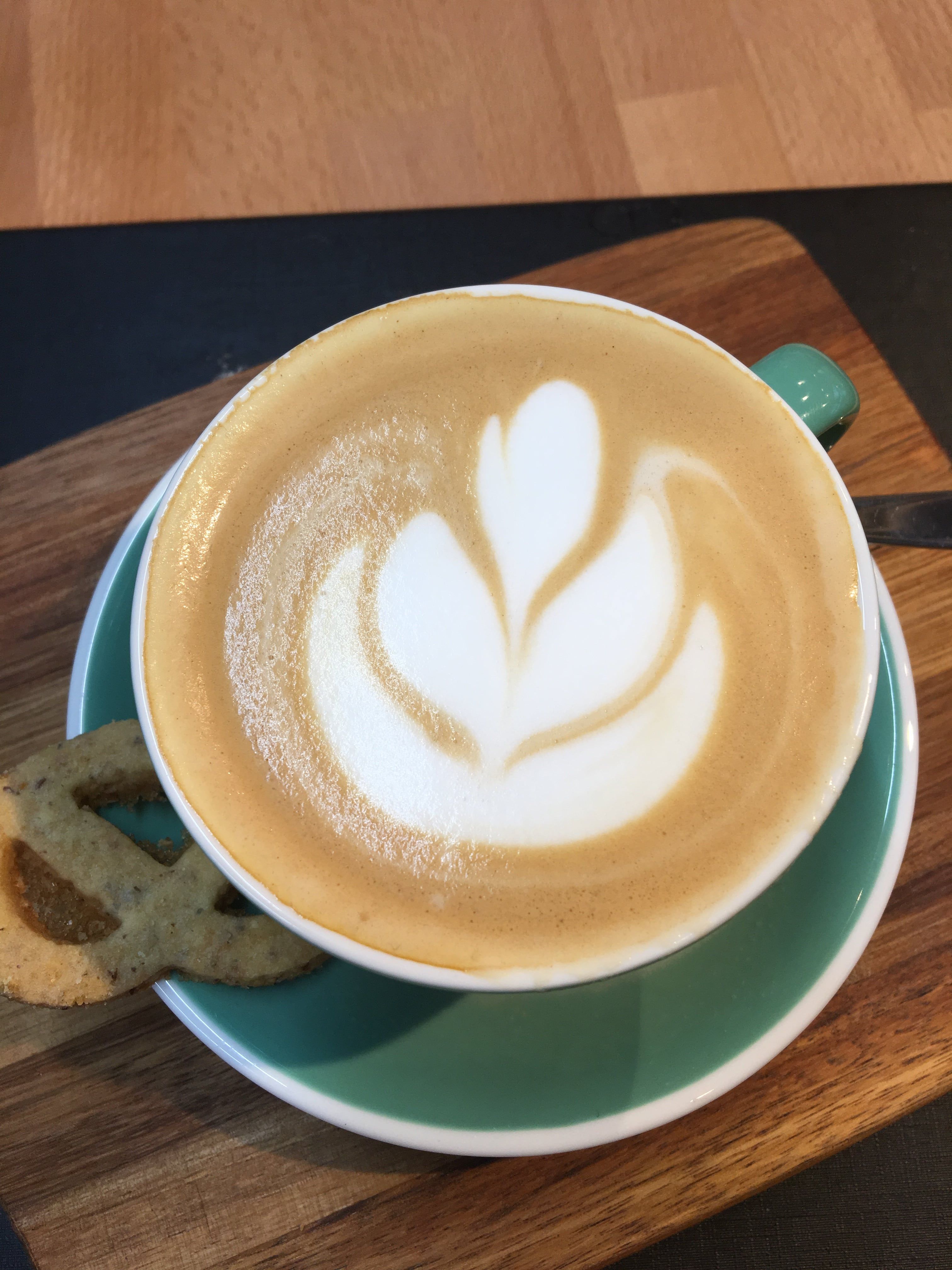 Cappuccino s latte art v zelenom pohári na drevenej doske.