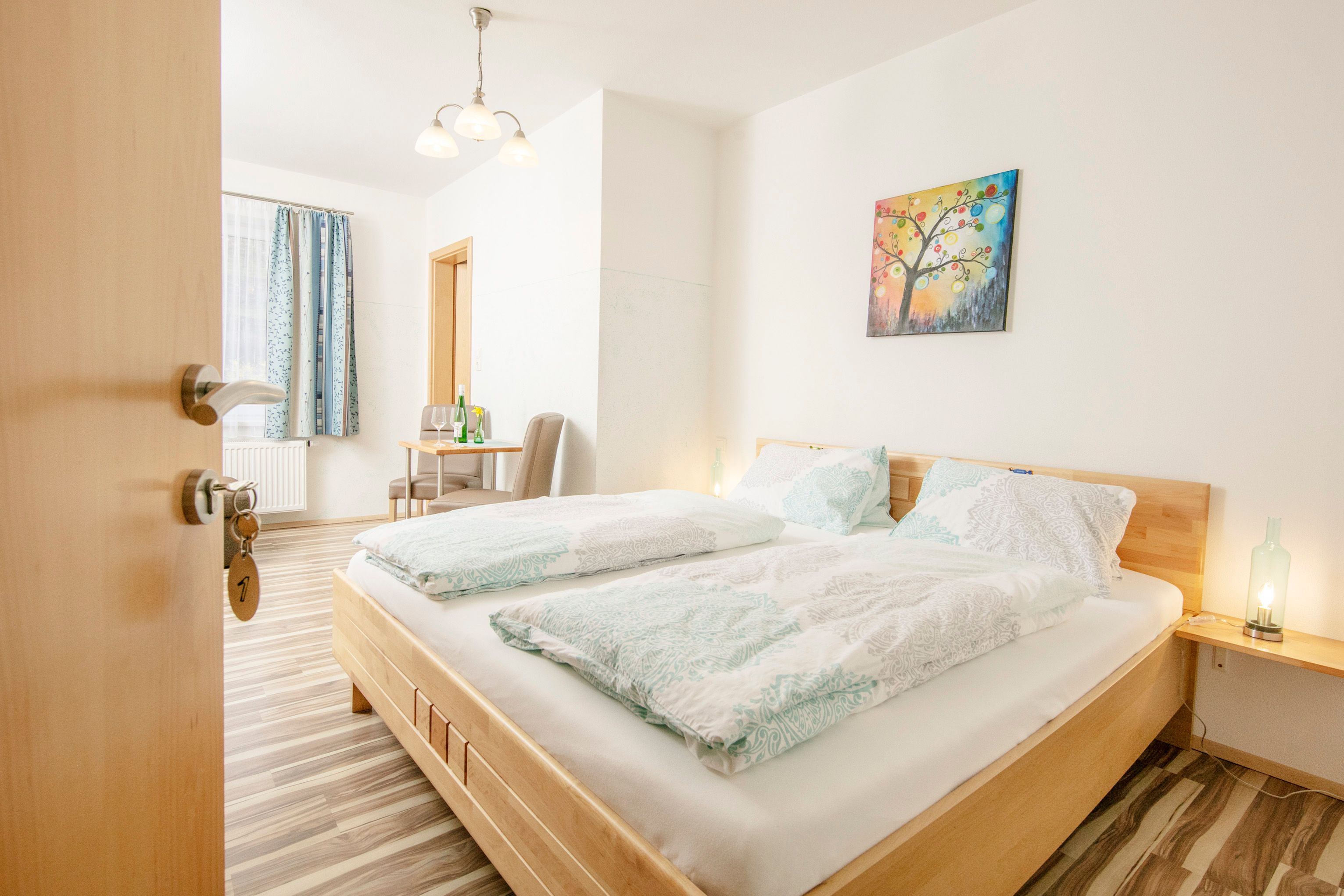 Svetlá izba pre hostí s manželskou posteľou, stolom, stoličkami a farebnou nástennou maľbou.