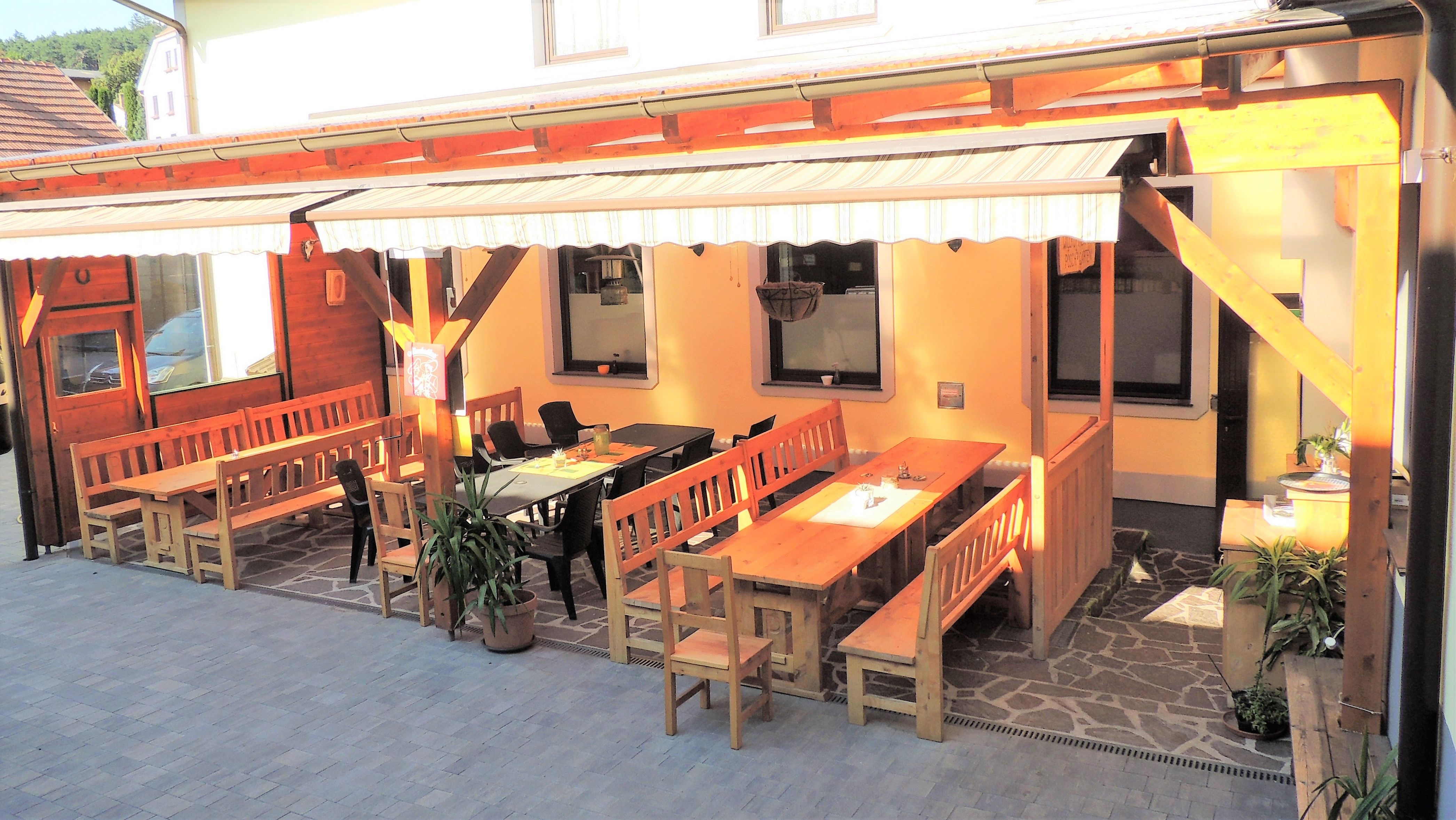 Útulná záhrada pre hostí s drevenými lavičkami a stolmi pod prístreškom.