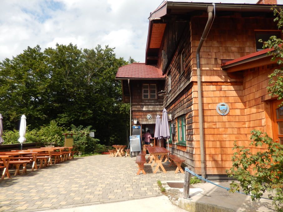 Drevená chatka s terasou a vonkajšími lavičkami.