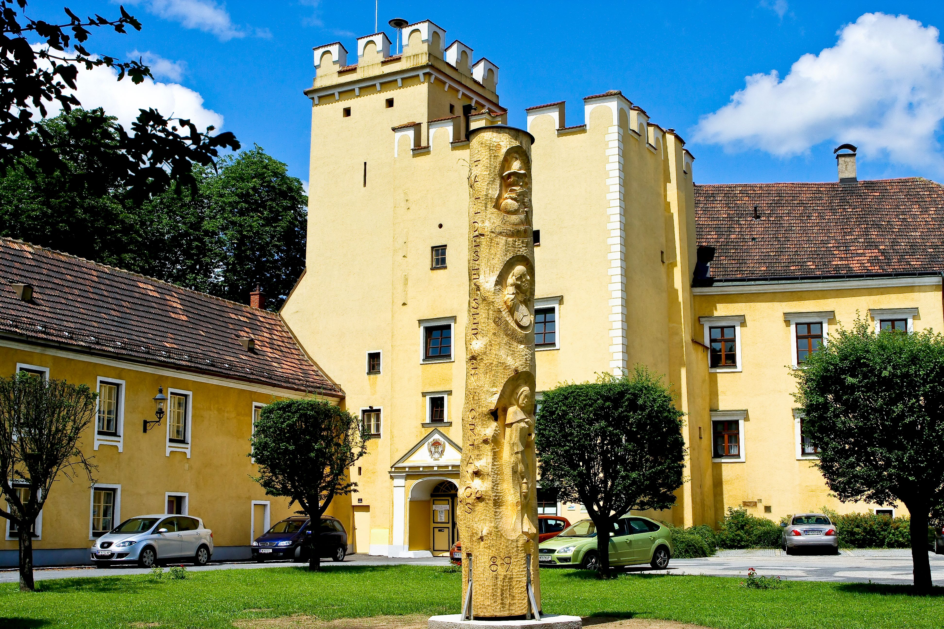 Žltá budova s vežou a zlatou sochou v popredí.