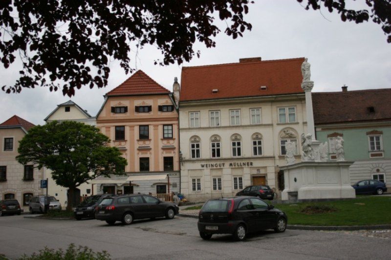 Historické budovy s nápisom "Weingut Müllner" a socha na námestí.