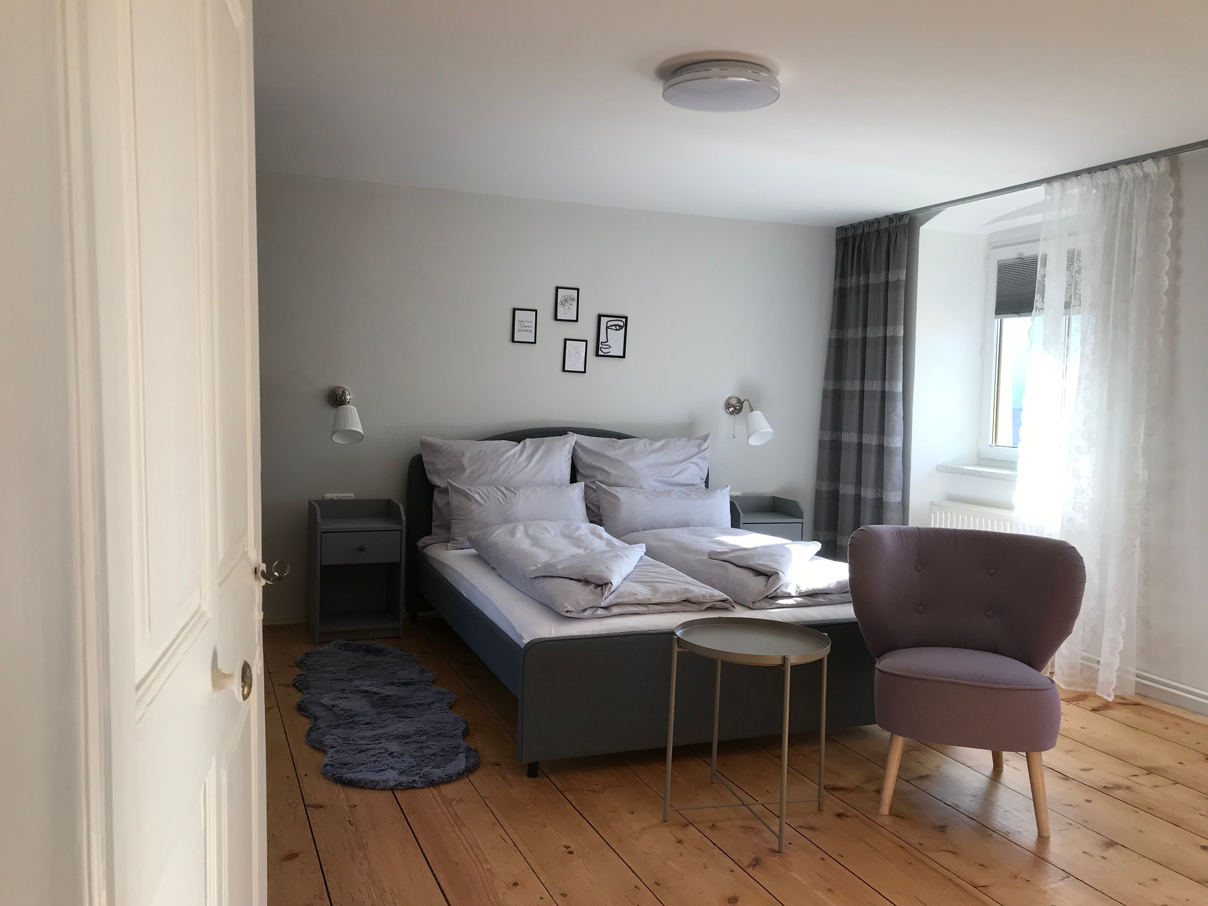 Moderne zariadená dvojlôžková izba s posteľou, kreslom a stolíkom na drevenej podlahe.