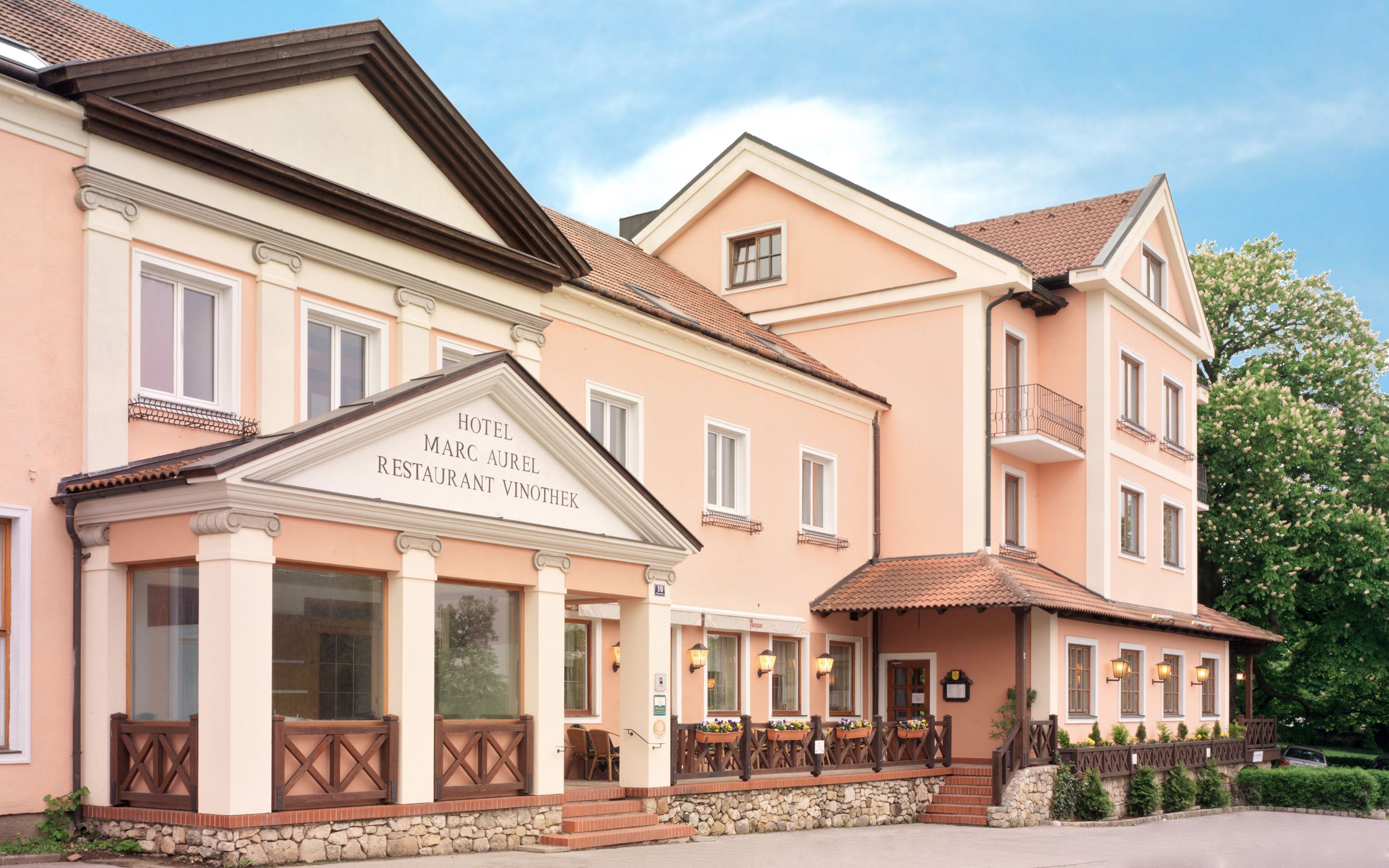 Exteriérový pohľad na hotel Marc Aurel v Petronell-Carnuntum s ružovou fasádou a klasickým vchodom.