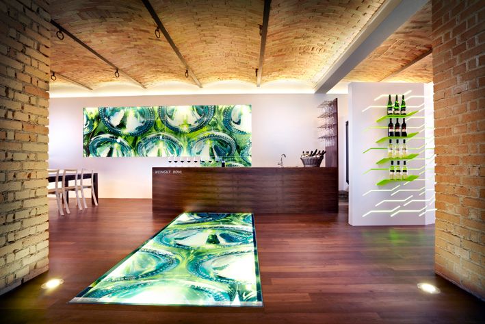 Moderný interiér vinárstva s osvetlenou podlahou a fľašami vína na stene.