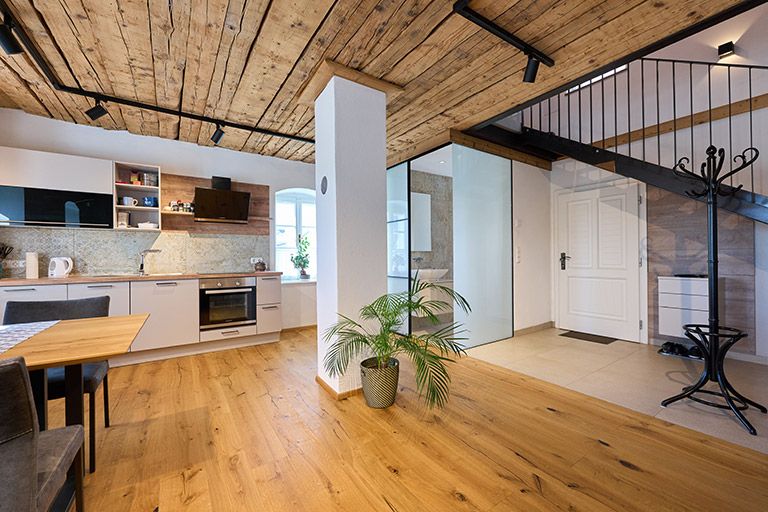 Moderná kuchyňa s drevenou podlahou a stropom, schodisko a rastliny.