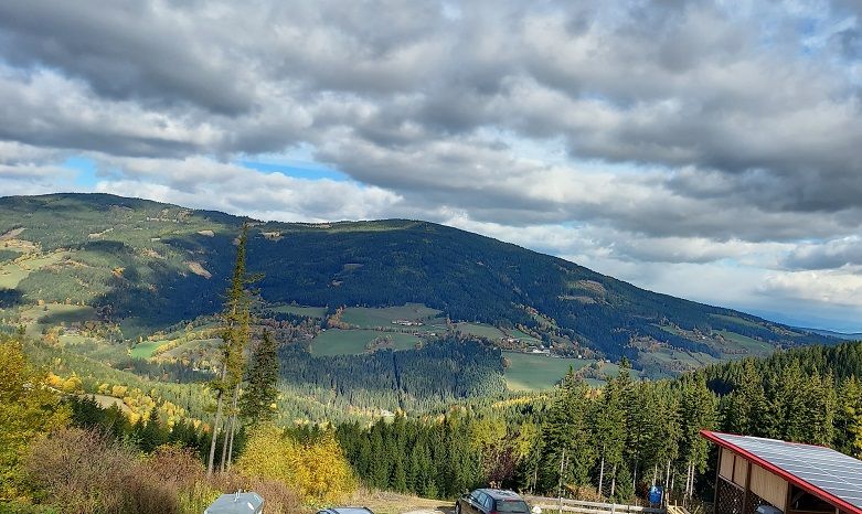 Panoramatický pohľad na kopcovitú krajinu s lesmi a poľami pod zamračenou oblohou.