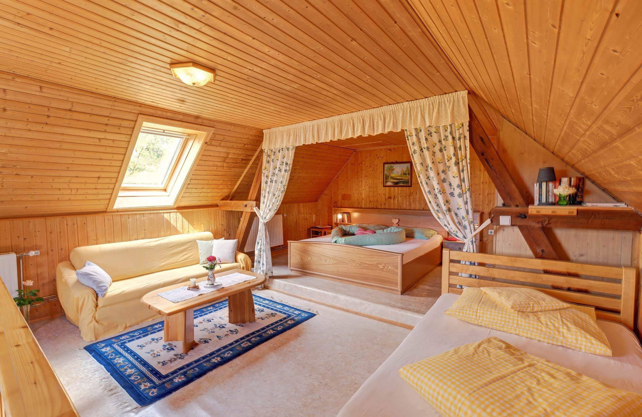 Útulná spálňa s drevenými stenami, posteľou, pohovkou a strešným oknom.