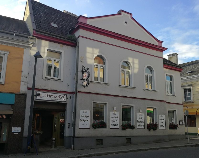 Hostinec s nápisom "Wirt am Eck" na rohu ulice.