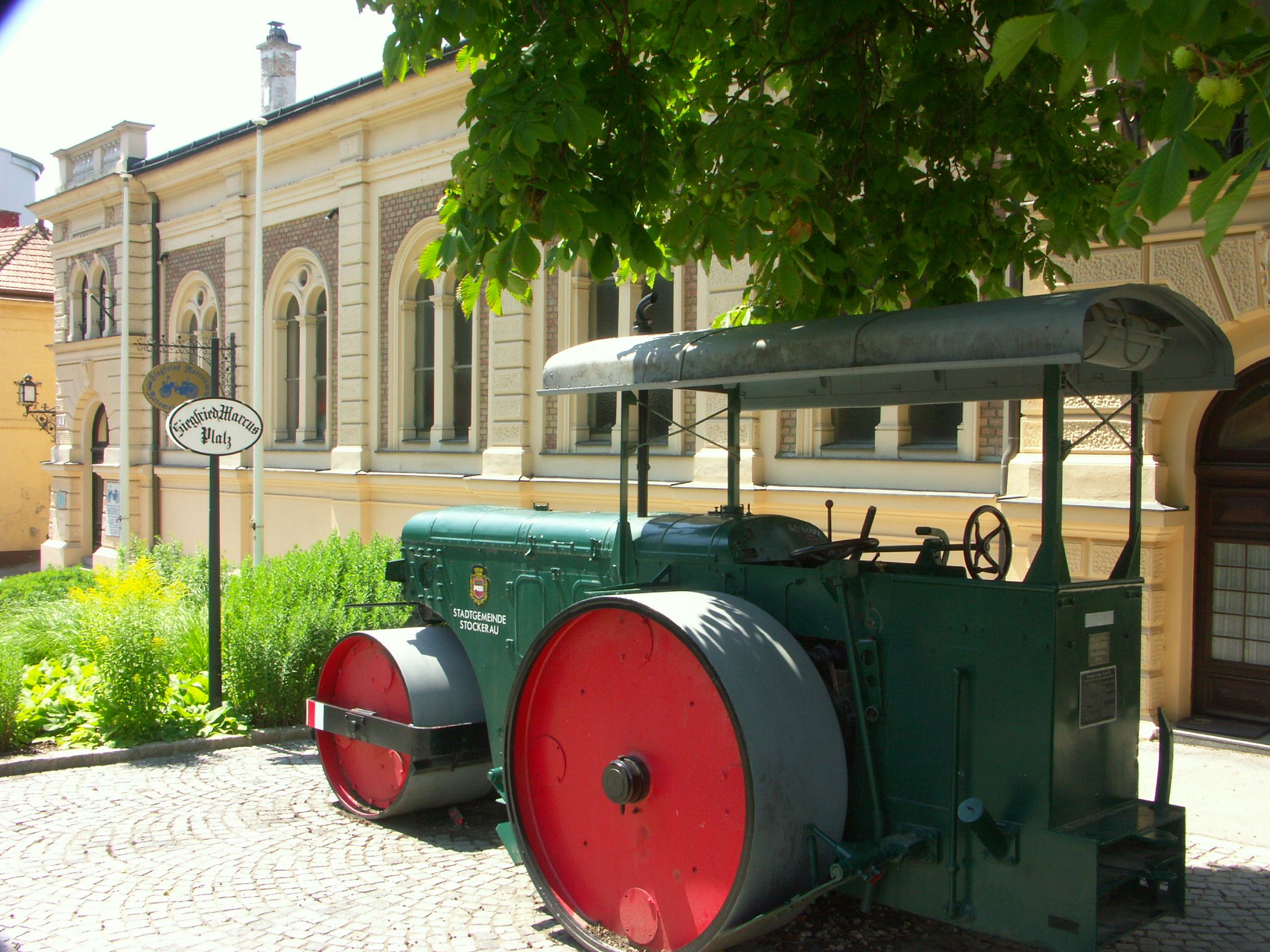 Historický parný valec pred budovou s nápisom "Siegfried Marcus Platz".