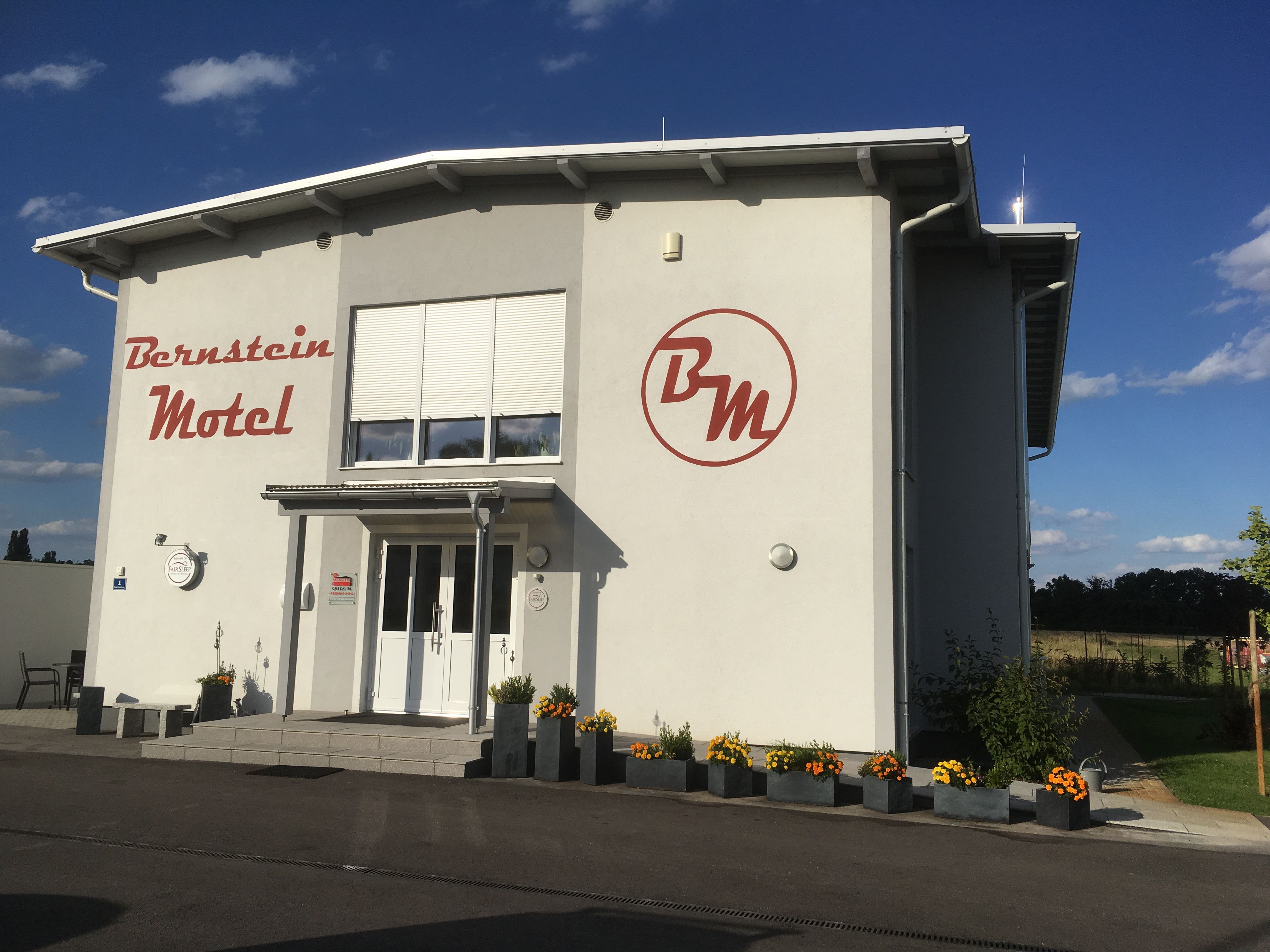 Exteriérový pohľad na motel Bernstein s kvetmi a modrou oblohou.