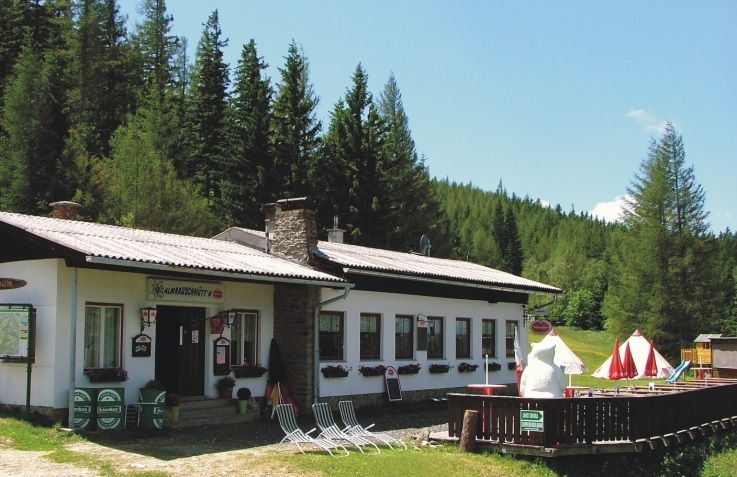 Chata Almrausch v lesnej krajine so slnečníkmi a ležadlami.