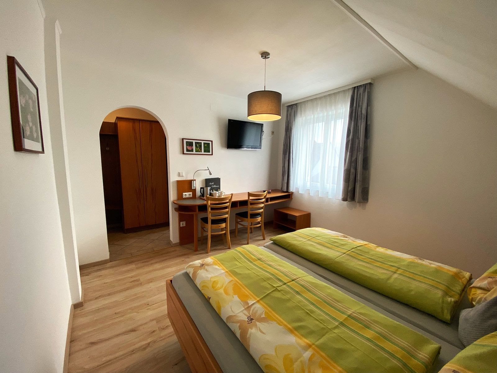 Útulná dvojlôžková izba s dvoma posteľami, písacím stolom, stoličkami a TV na stene.