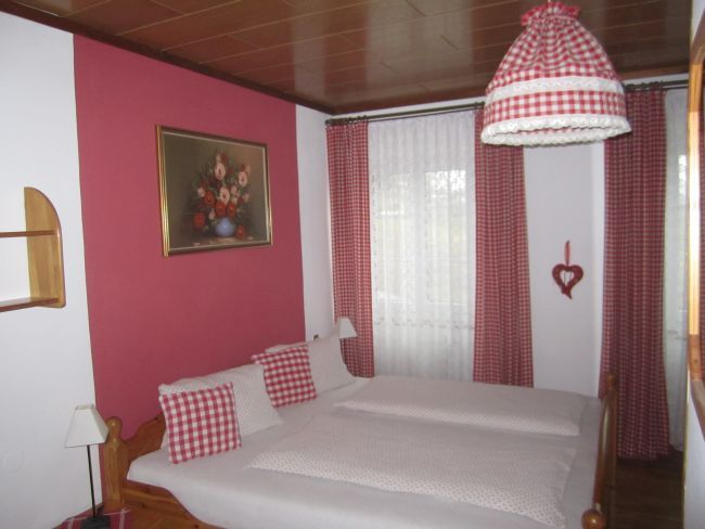 Spálňa s červeno-bielymi kockovanými závesmi a posteľnou bielizňou.